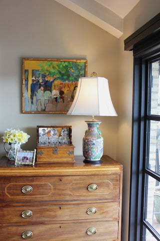 Wooden dresser with a lamp, vase, and framed photos against a wall with a painting.