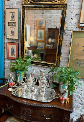 Vintage interior with ornate mirror, wooden dresser, and decorative items against a brick wall.