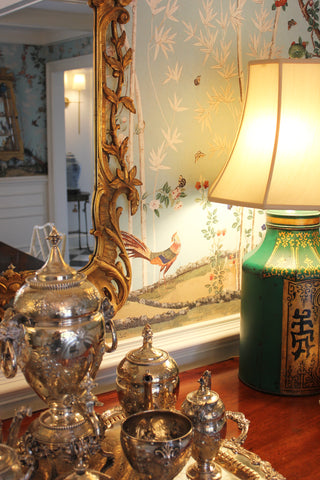 Decorative table setting with silver urns, a green lamp, and a mirror with floral design.
