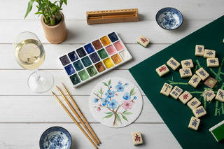 Watercolor paints, brushes, and mahjong mat with tiles flat lay